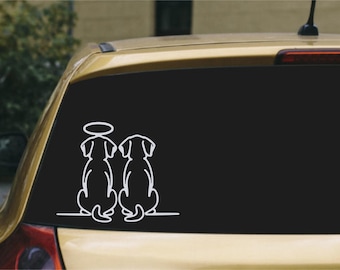 May include: A white vinyl decal applied to a car window featuring a line art illustration of two dogs sitting side by side. One dog is positioned on the left and has a halo floating above its head, while the other dog sits on the right.