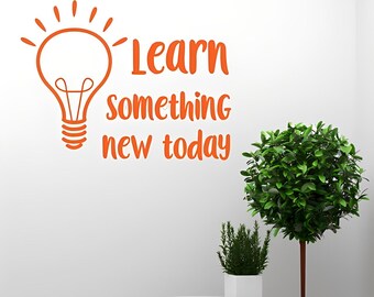 May include: An orange wall decal featuring a line-art light bulb icon with rays at the top and the text "Learn something new today" in a rounded, sans-serif font. The design is applied to a plain white wall surface for clear visibility.