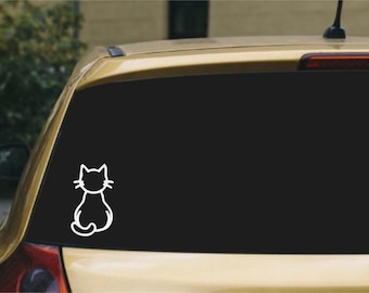 May include: A white vinyl decal featuring a simple line art illustration of a cat sitting with its back turned, applied to the rear window of a gold-colored vehicle. The cat design shows pointed ears, whiskers, and a curled tail in a minimalist style.