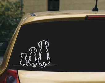 May include: A white vinyl decal applied to a car window featuring a continuous line art illustration of a cat and two dogs sitting side by side, all facing away from the viewer. The design is composed of simple, clean white outlines.