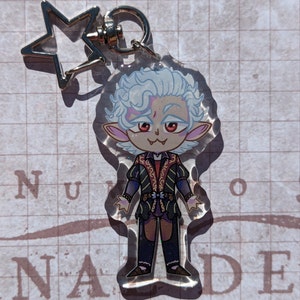 May include: A clear acrylic keychain featuring a cartoon character with white hair, red eyes, and a mischievous grin. The character is wearing a dark green and gold outfit with a red sash. The keychain is attached to a silver star-shaped charm.