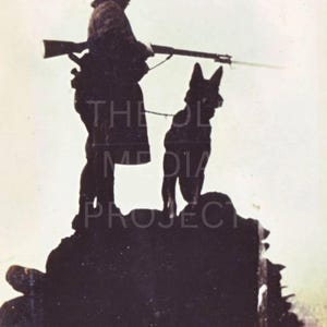 May include: Silhouette of a person holding a rifle, standing with a dog on a rocky surface. The person is wearing a hat and coat. The dog is a German Shepherd. The image is in black and white.