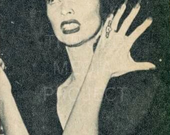 May include: Black and white vintage photograph of a woman with dark hair and dramatic makeup. She has long fingernails and is wearing a ring. The image has text that is partially visible. The woman is looking up and to the left with an intense expression.