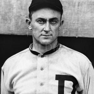 May include: Black and white portrait of a man wearing a baseball uniform. He is wearing a black cap with a white "D" on it and a light-colored jersey with a large black "D" on the chest. The man has a serious expression.