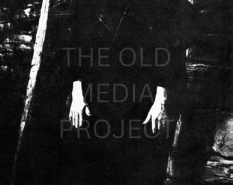 Może przedstawiać: Czarno-białe zdjęcie mężczyzny w ciemnym płaszczu, z bladą twarzą i ciemnymi włosami. Obraz ma tekst "THE OLD MEDIA PROJECT" na środku. Mężczyzna stoi na tle ciemnego tła.