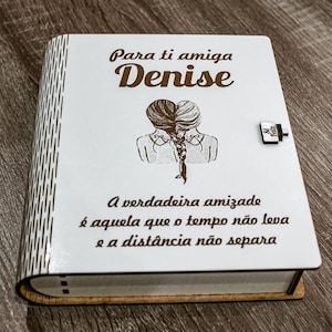Pode incluir: Uma caixa de madeira branca com uma inscrição marrom que diz "Para ti amiga Denise" e "A verdadeira amizade é aquela que o tempo não leva e a distância não separa". A caixa tem uma pequena fechadura e uma fechadura.