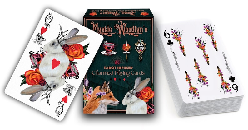 Może przedstawiać: Talia kart do gry w zielonym, czarnym i złotym pudełku. Pudełko przedstawia lisa i kr&oacute;lika z kwiatowymi akcentami. Tekst na pudełku brzmi "Mystic Woodlyn's Tarot Infused Charmed Playing Cards".