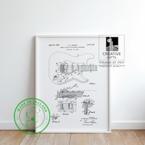 Può includere: Stampa in bianco e nero incorniciata di un diagramma di brevetto di chitarra. La stampa include schemi dettagliati e testo, con un timbro verde "Made in Ireland" e un logo "Creative Gifts", il tutto in una cornice bianca.