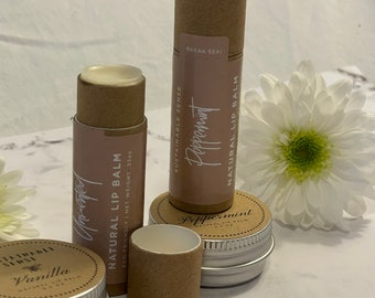 May include: Three natural lip balms in different flavors: peppermint, vanilla, and peppermint. The balms are in cardboard tubes and metal tins. The tubes are brown and have white text. The tins are silver and have white text. The balms are on a white marble surface.