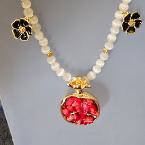 May include: A white beaded necklace with a gold pomegranate pendant and two black flower charms.