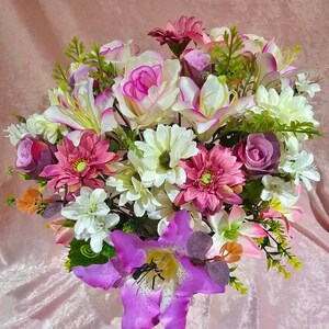 May include: A bouquet of pink, white and purple artificial flowers in a vase. The flowers include lilies, daisies and roses.