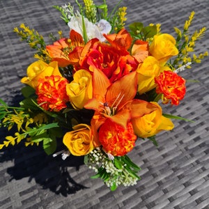 May include: A bouquet of artificial flowers in shades of orange, yellow, and white. The flowers are arranged in a vase and include lilies, roses, and carnations.