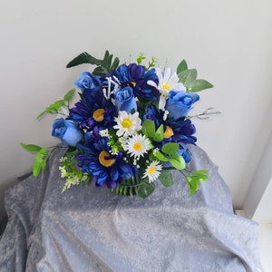 May include: A bouquet of artificial flowers in shades of blue and white. The bouquet features blue roses and daisies with white centres.