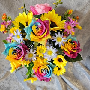 May include: A bouquet of colourful artificial flowers, including rainbow roses, sunflowers, and daisies. The flowers are arranged in a vase and are displayed on a grey background.