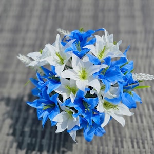 May include: A bouquet of white and blue lilies. The lilies are arranged in a circular shape and are tied together with a ribbon.
