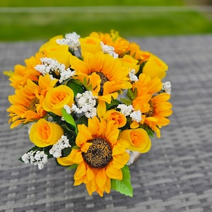May include: A bouquet of yellow sunflowers and white baby's breath arranged in a floral arrangement.