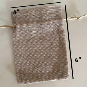 Op de afbeelding: Een klein, beige jute trekkoordtasje met een afmeting van 10 cm bij 15 cm. De tas heeft een natuurlijke, rustieke uitstraling en is perfect voor kleine cadeautjes of attenties.