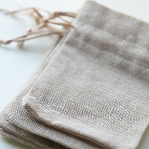 Op de afbeelding: Een stapel van drie natuurlijke linnen trekzakjes. De zakjes zijn gemaakt van een zachte, geweven stof en hebben een natuurlijke beige kleur.
