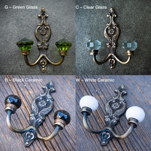 May include: Decorative wall hooks with ornate metalwork and various knob options. The image shows hooks with green glass, clear glass, black ceramic, and white ceramic knobs. Each hook has two knobs and a decorative backplate.