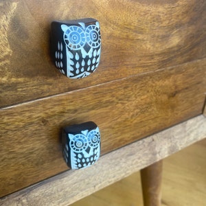 May include: Two wooden drawer pulls shaped like owls with white painted details. The owl on the top drawer is larger than the owl on the bottom drawer.