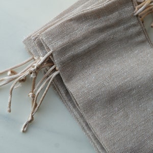Op de afbeelding: Een stapel kleine, natuurlijke kleur jute trekkoordzakken met een natuurlijke kleur touw trekkoord.
