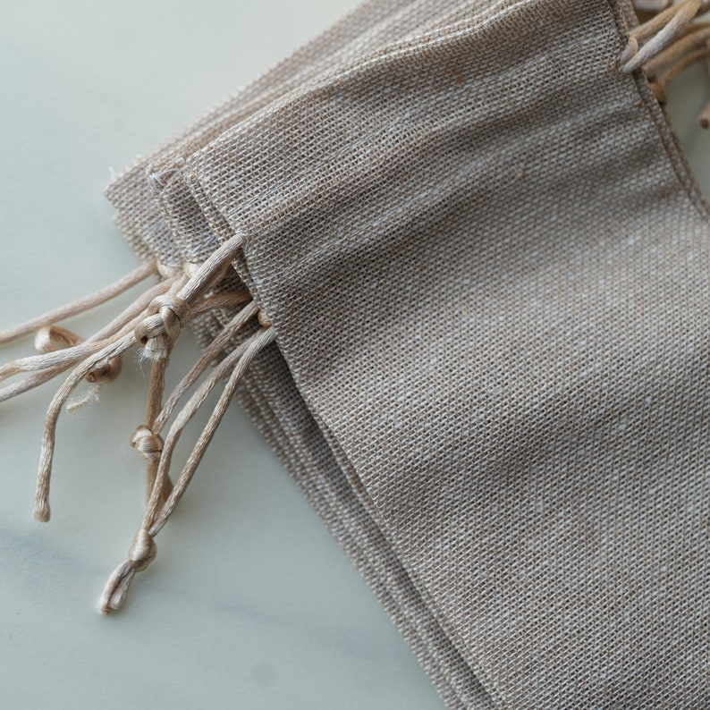 Op de afbeelding: Een stapel kleine, natuurlijke kleur jute trekkoordzakken met een natuurlijke kleur touw trekkoord.