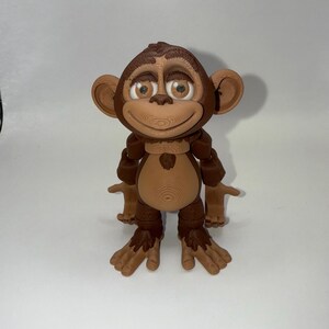 May include: A 3D-printed monkey figurine with a smiling expression. The monkey has brown fur, large ears, and light brown eyes. Its arms and legs are outstretched, and it has a detailed, textured surface.