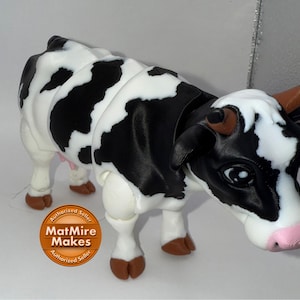 May include: A 3D-printed cow figurine with a black and white spotted pattern. The cow has brown hooves and horns, a pink nose, and large, expressive eyes. The figurine is a decorative item, possibly a toy or collectible.