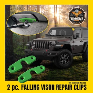 Peut inclure: Clips de réparation de visière tombante verts. L'image montre deux clips verts, dont un installé sur un pare-soleil de voiture. Le texte sur l'image indique "2 pc. FALLING VISOR REPAIR CLIPS". L'arrière-plan présente une Jeep et une forêt.