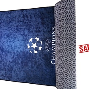 Puede incluir: Una alfombra azul y blanca con un bal&oacute;n de f&uacute;tbol y las palabras "UEFA CHAMPIONS" impresas en ella. La alfombra est&aacute; enrollada y tiene un patr&oacute;n de diamantes en la parte posterior.