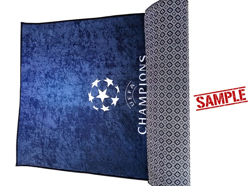 Puede incluir: Una alfombra azul y blanca con un bal&oacute;n de f&uacute;tbol y las palabras "UEFA CHAMPIONS" impresas en ella. La alfombra est&aacute; enrollada y tiene un patr&oacute;n de diamantes en la parte posterior.