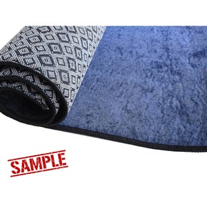 Puede incluir: Una alfombra enrollada con un patr&oacute;n geom&eacute;trico blanco y negro en un lado y un color azul s&oacute;lido en el otro lado. La alfombra tiene un borde negro.
