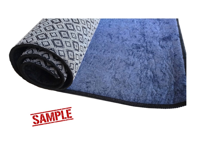 Puede incluir: Una alfombra enrollada con un patr&oacute;n geom&eacute;trico blanco y negro en un lado y un color azul s&oacute;lido en el otro lado. La alfombra tiene un borde negro.