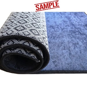 Puede incluir: Una alfombra enrollada con un patr&oacute;n geom&eacute;trico blanco y negro en un lado y un color azul s&oacute;lido en el otro lado. La alfombra tiene un borde negro.