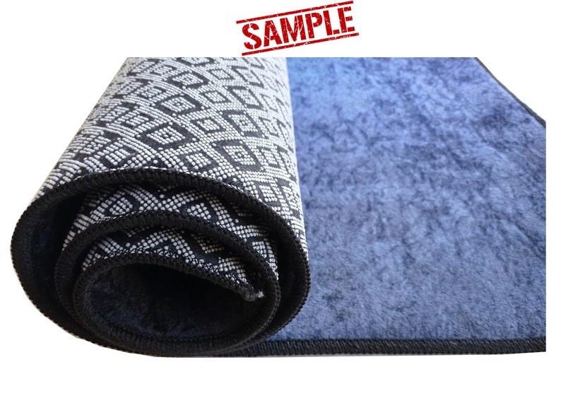 Puede incluir: Una alfombra enrollada con un patr&oacute;n geom&eacute;trico blanco y negro en un lado y un color azul s&oacute;lido en el otro lado. La alfombra tiene un borde negro.