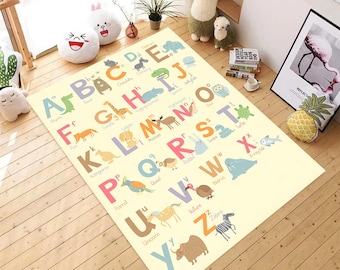 May include: A rectangular, cream-colored children's rug featuring the alphabet with colorful animal illustrations. Each letter is paired with an animal, such as "A" for alligator and "Z" for zebra. The rug is placed on a wooden floor.