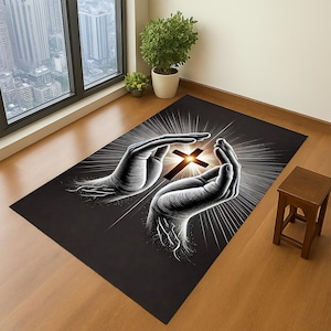 May include: A rectangular black rug featuring a detailed illustration of two hands cradling a glowing cross. White rays emanate from the cross, creating a halo effect. The rug is placed on a wooden floor.