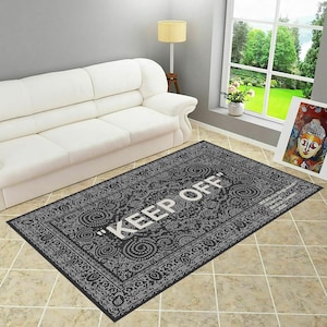 May include: A black and white patterned rug with the text "KEEP OFF" in white lettering. The rug is on a tiled floor in front of a white couch.