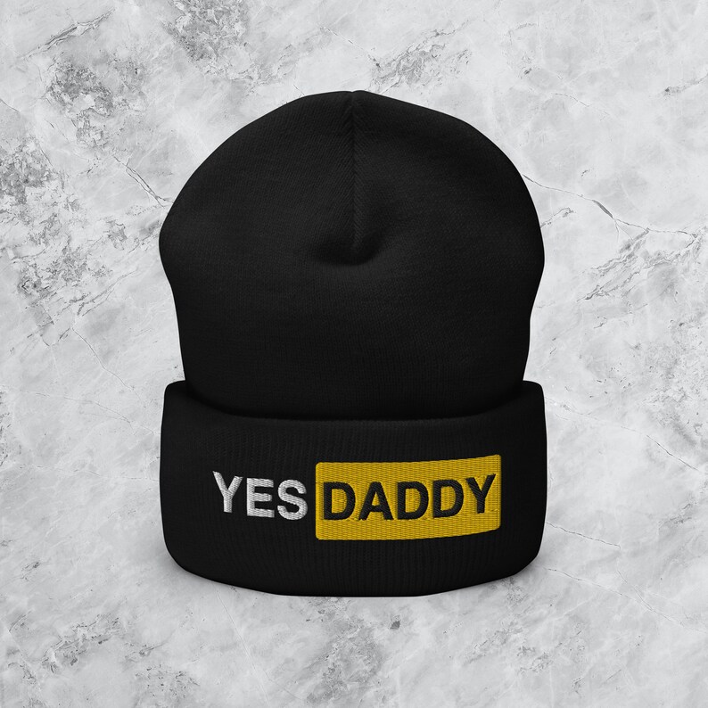 Może przedstawiać: Czarna czapka z daszkiem z ż&oacute;łtym prostokątem, na kt&oacute;rym widnieje napis "YES DADDY" białymi literami.
