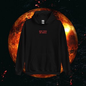 Op de afbeelding: Zwart hoodie met de tekst "SEE YOU IN HELL" in rode letters op de voorkant.