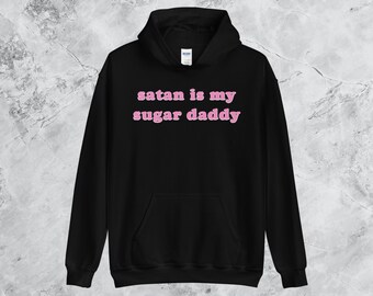 Könnte beinhalten: Schwarzer Kapuzenpullover mit dem Text "satan is my sugar daddy" in rosa Buchstaben.