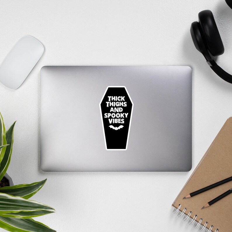 May include: Black and white sticker with a coffin shape and the text "Thick Thighs and Spooky Vibes" with a bat graphic.