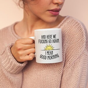 Puede incluir: Taza de caf&eacute; de cer&aacute;mica blanca con un gr&aacute;fico negro y amarillo de un sol y el texto "And here we fucking go again. I mean good morning."