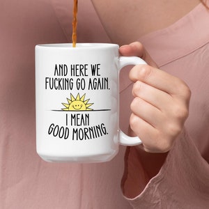 Puede incluir: Taza de caf&eacute; blanca con texto negro que dice "And here we fucking go again. I mean good morning." Un sol amarillo con una cara sonriente est&aacute; sobre el texto.