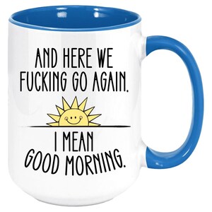 Pode incluir: Caneca de caf&eacute; branca com borda e al&ccedil;a azuis. A caneca tem um gr&aacute;fico preto de um sol com um rosto sorridente e o texto "And here we fucking go again. I mean good morning."