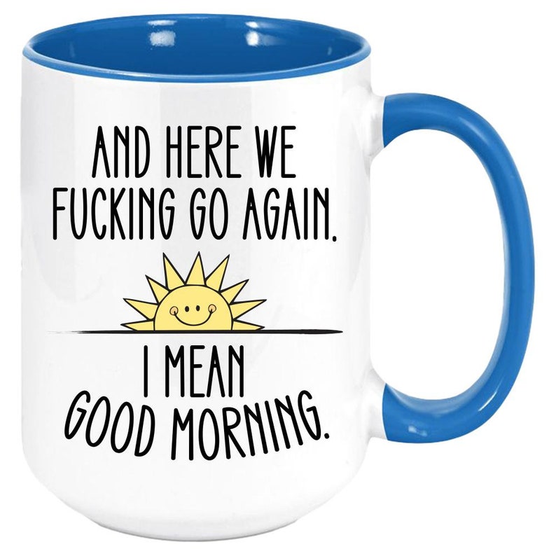 Pode incluir: Caneca de caf&eacute; branca com borda e al&ccedil;a azuis. A caneca tem um gr&aacute;fico preto de um sol com um rosto sorridente e o texto "And here we fucking go again. I mean good morning."