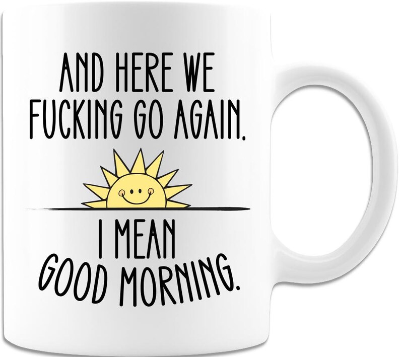 Puede incluir: Taza de caf&eacute; blanca con texto negro que dice "And here we fucking go again. I mean good morning." Un sol amarillo con una cara sonriente est&aacute; sobre el texto.