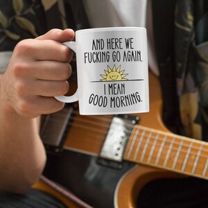 Pode incluir: Caneca de caf&eacute; branca com texto preto que diz "And here we fucking go again. I mean good morning." com um gr&aacute;fico de sol amarelo.