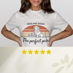 May include: White t-shirt with a graphic design featuring a dog sitting on books, with the text "DOGS AND BOOKS" above and "The perfect pair" below. The design includes a retro sunset.