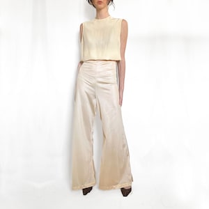 May include: A cream-colored sleeveless top with a scoop neck and wide-leg pants. The pants have a high waist and a wide leg.
